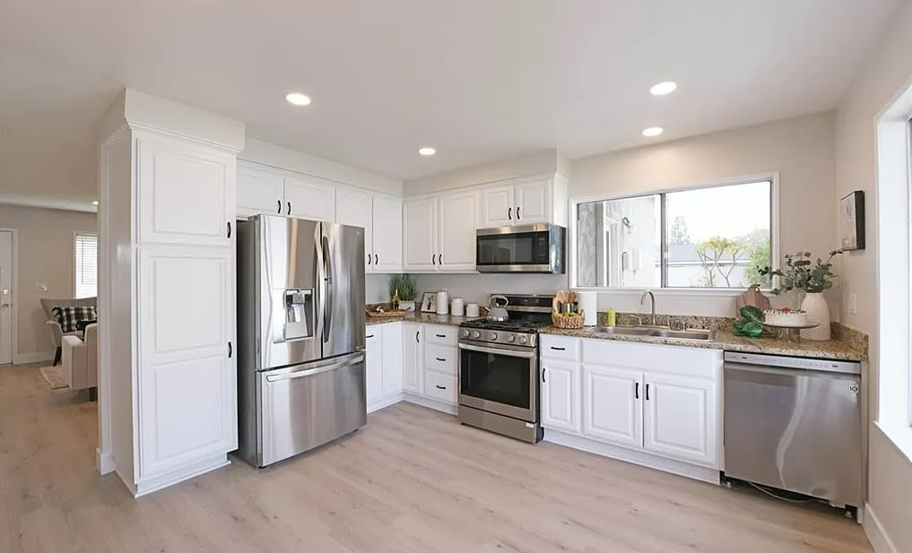 Renovated kitchen with white cabinets, stainless steel appliances, granite counters, and a large window.