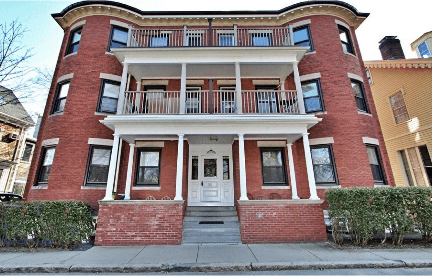 Red brick building with stacked balconies, white columns, and a central front entrance.