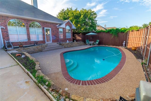 Backyard swimming pool with curved brick coping beside a brick house and fenced patio.