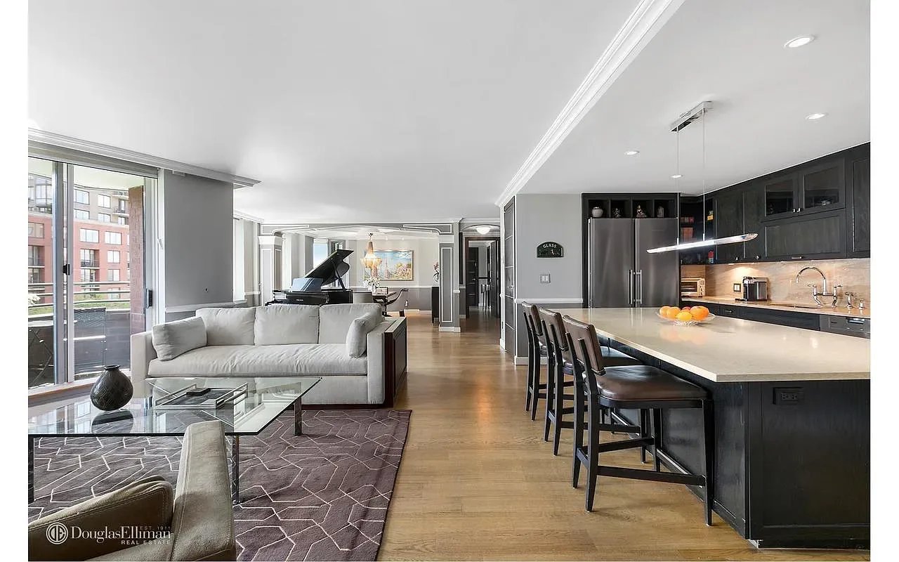 Open-plan living room and kitchen with a dark island, gray sofa, grand piano, and balcony windows.