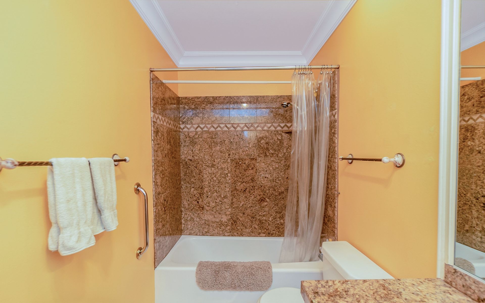 Bathroom with a white bathtub, brown marbled shower surround, and yellow walls.