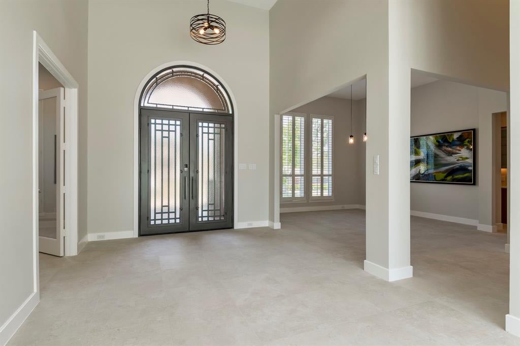 Empty entry foyer with an arched glass double door, pale tile floors, and a sculptural pendant light.