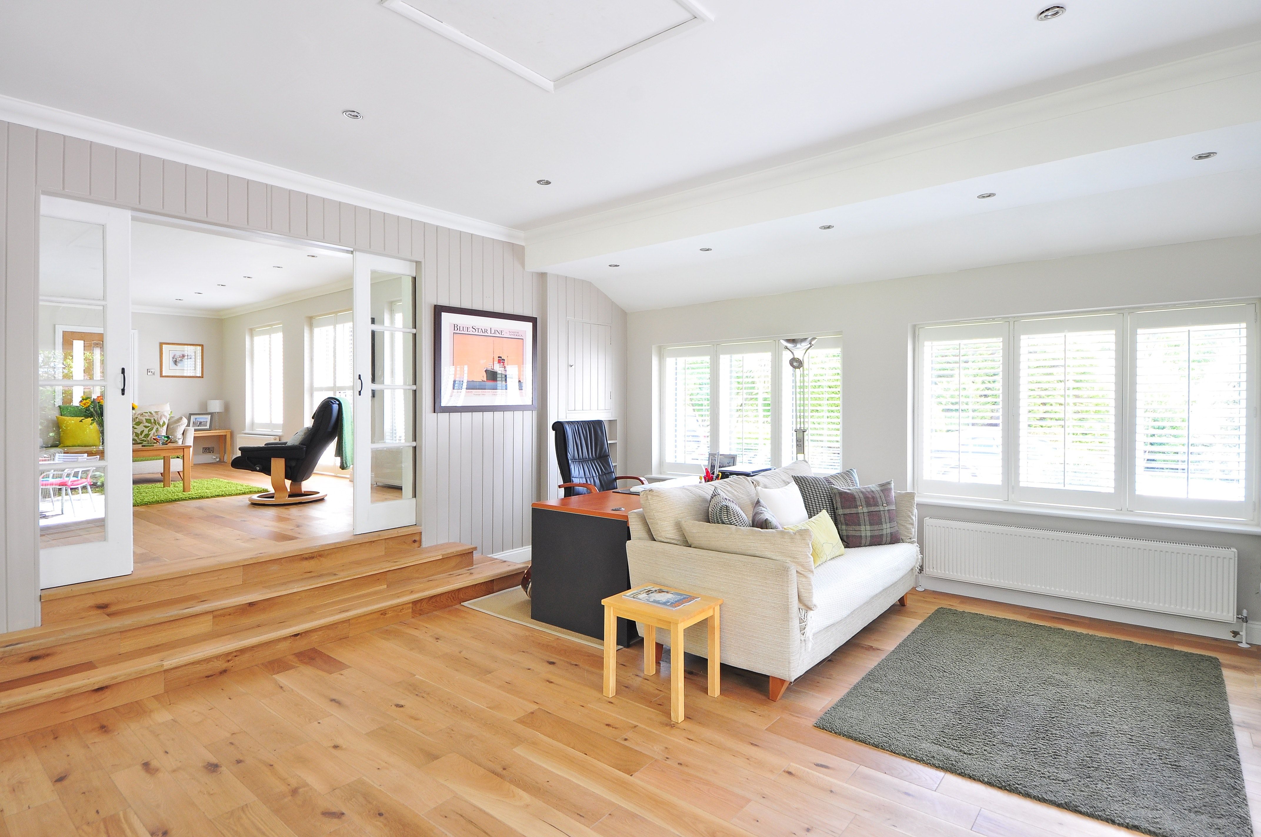 Bright living room with a cream sofa, shuttered windows, and wooden steps to an adjoining sitting area.