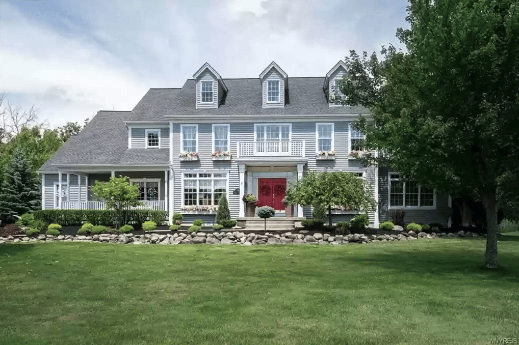 Gray two-story house with three dormers, a red front door, and a broad green lawn.