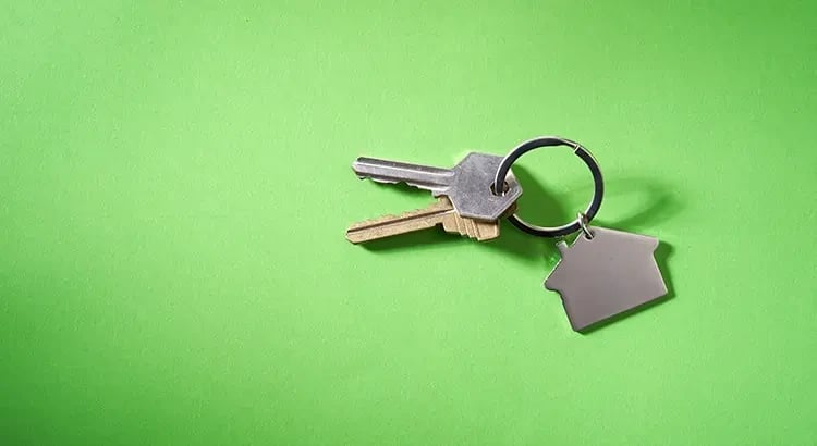 A set of keys with a house-shaped keychain against a bright green background. The image symbolizes real estate, home ownership, or renting.