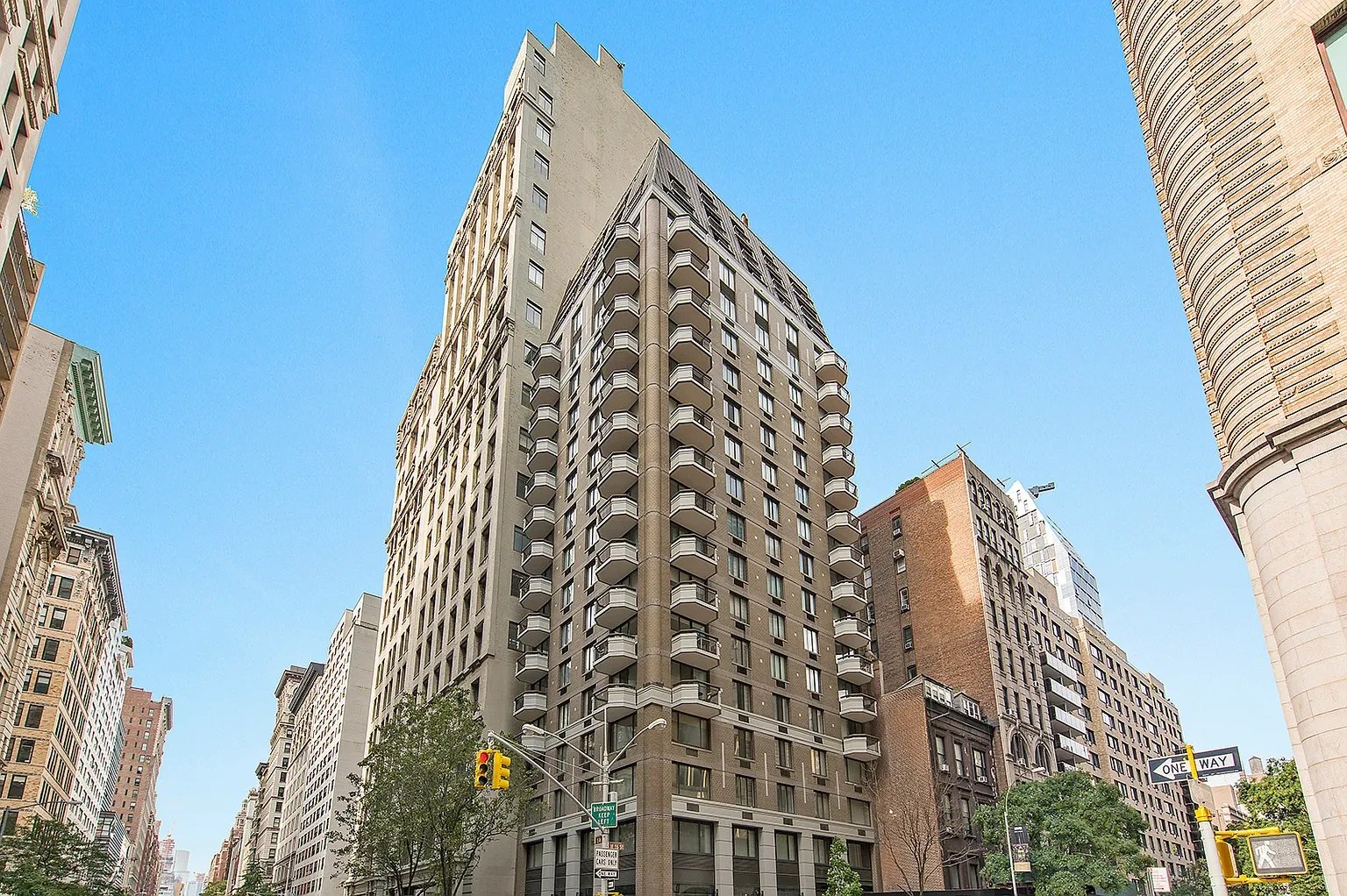 Tall beige residential building with rows of balconies on a sunny city street.