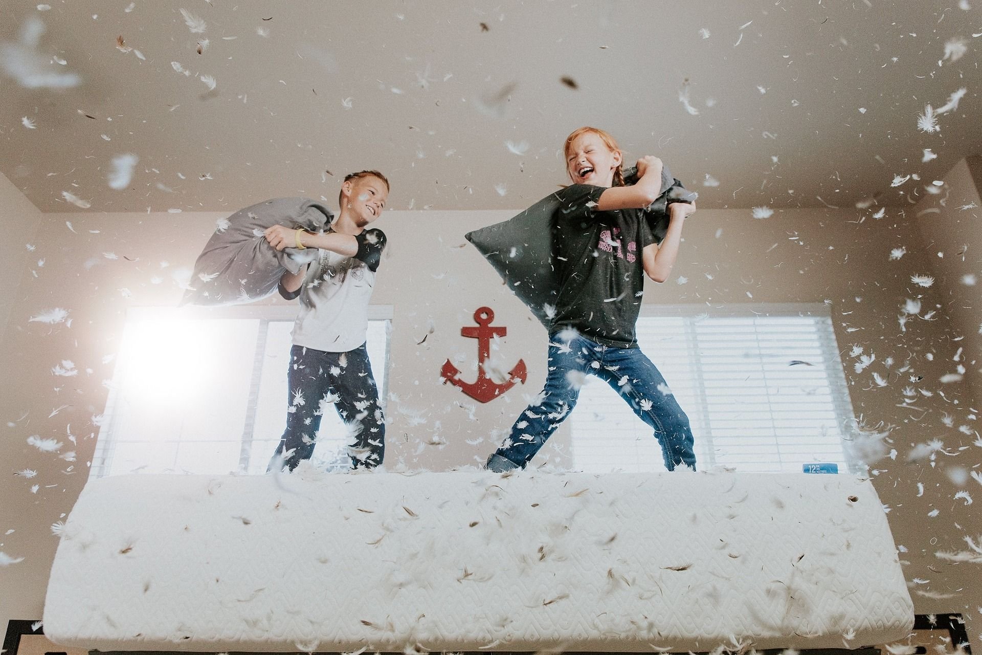 Two children have a playful pillow fight as feathers fly around them.