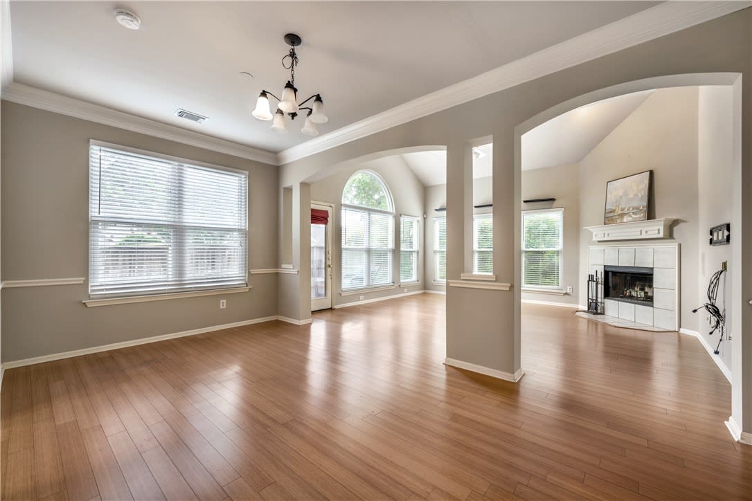 Vacant living room with hardwood floors, a tiled fireplace, and large arched windows.