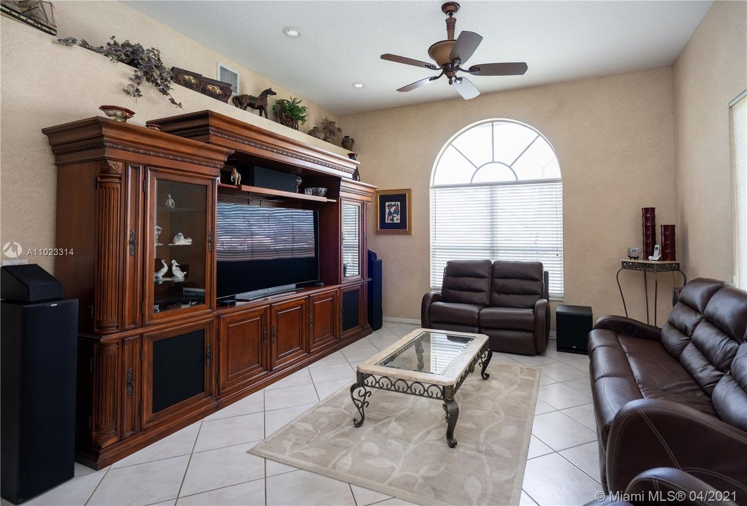 Living room with ornate wooden entertainment center, brown leather sofas, and an arched window.