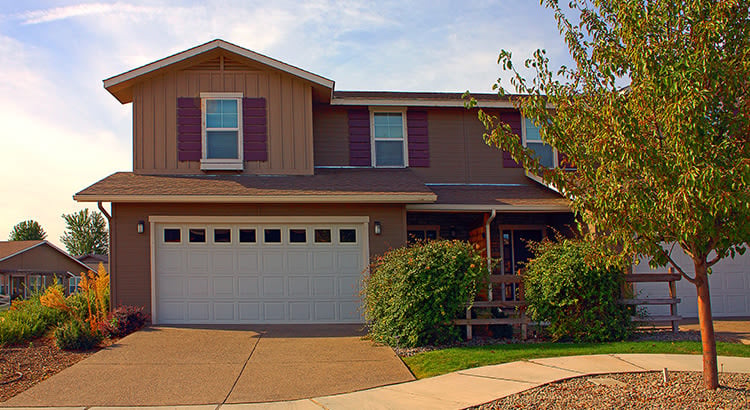 A two-story house with a driveway and some greenery.