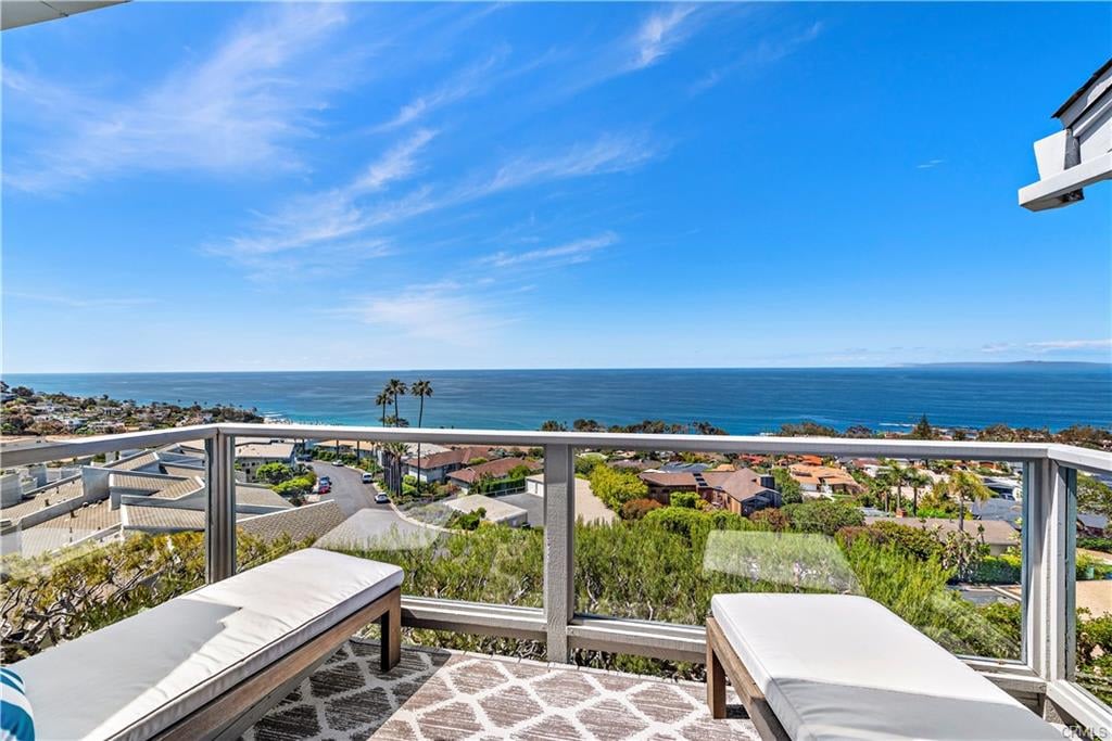 Balcony with lounge chairs overlooking the ocean and coastal homes.