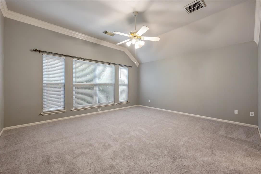 Empty bedroom with beige carpet, vaulted ceiling, ceiling fan, and three windows.