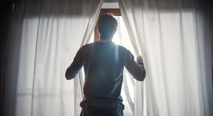 A man opening the curtains in his home