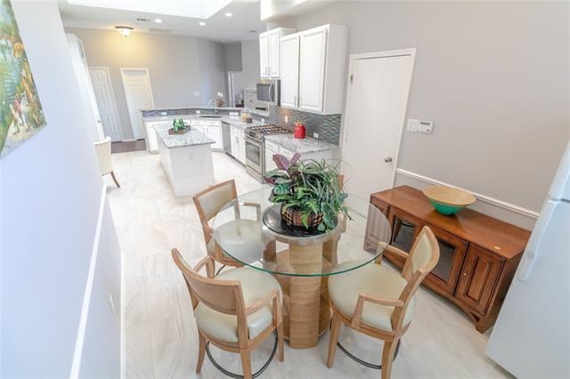 Dining area with a round glass table and wooden chairs beside a bright white kitchen.