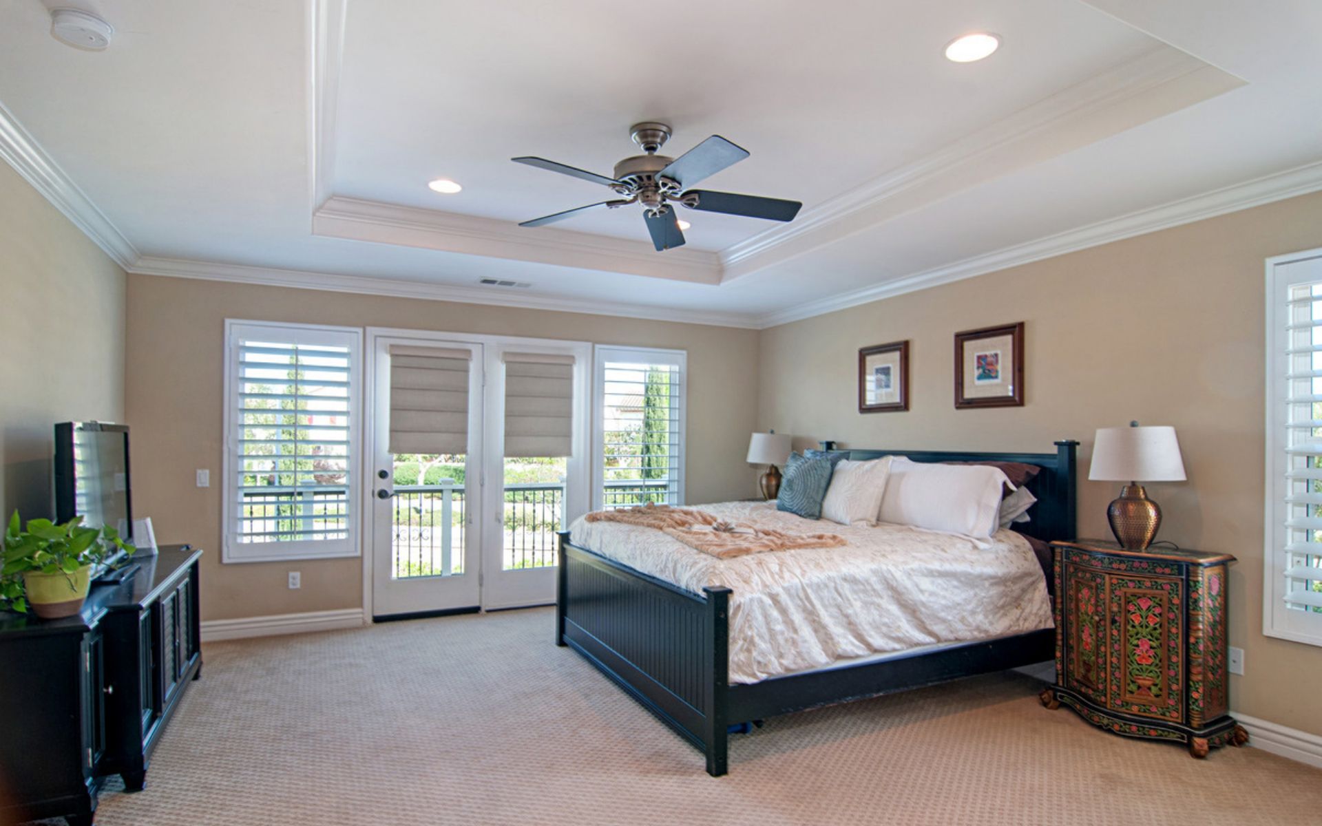 Bedroom with a large dark bed, ceiling fan, and French doors opening to a balcony.