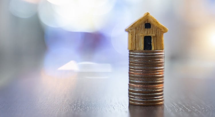 A small house model on top of a stack of coins, symbolizing real estate investment or financial planning related to housing.