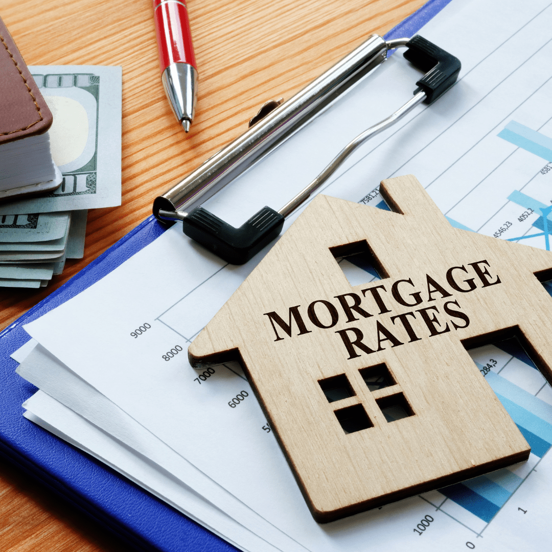 Wooden house labeled “MORTGAGE RATES” on financial charts beside cash and a pen.