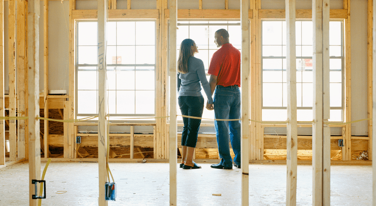 A couple standing inside a building under construction, possibly discussing the progress. The interior frame of the house is visible.