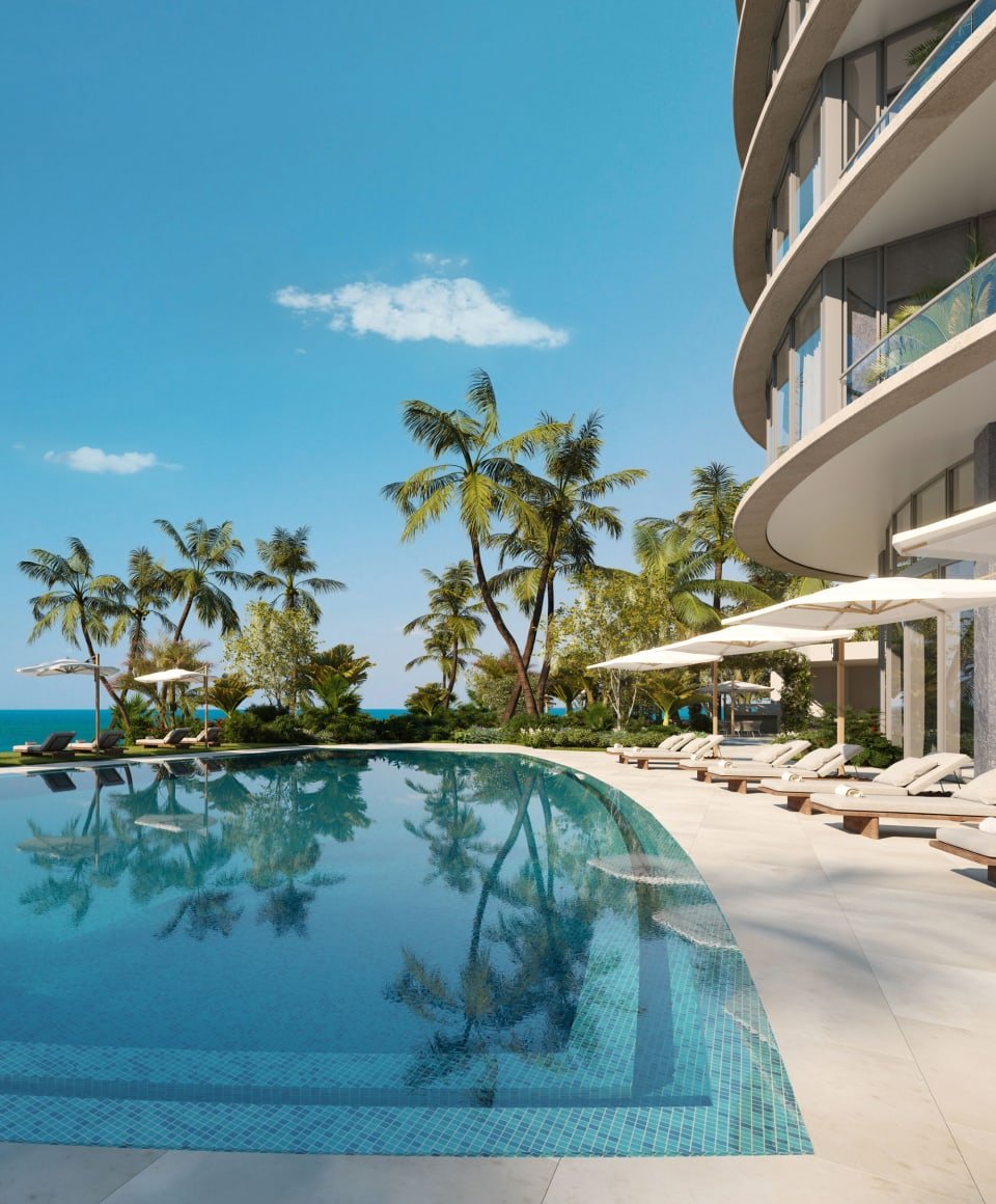 Rivage Bal Harbour residences beside a curved pool, with palm trees and ocean beyond.