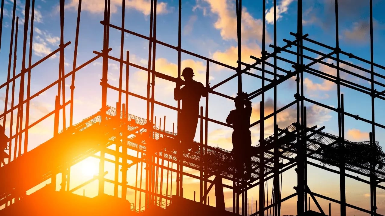A construction site with silhouetted workers at sunset. The image captures the ongoing building process and the effort involved.