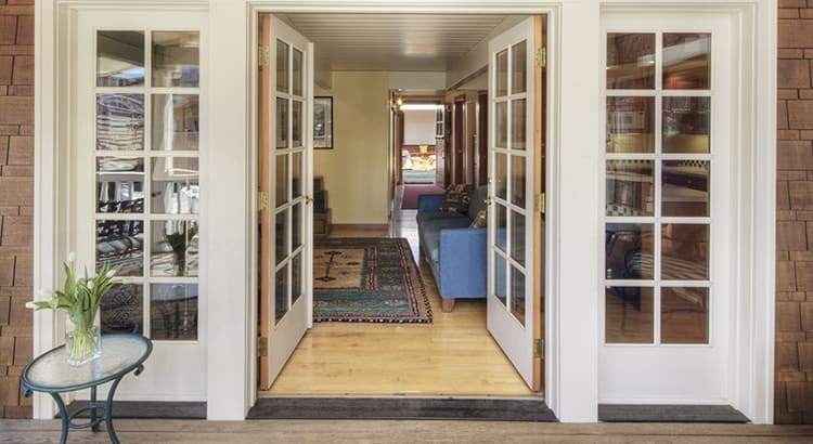 An interior view of a hallway in a house, featuring open double doors leading to another room. The space is well-lit and decorated with plants and furniture.