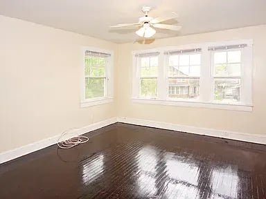 Empty room with dark hardwood floors, a ceiling fan, and multiple windows.