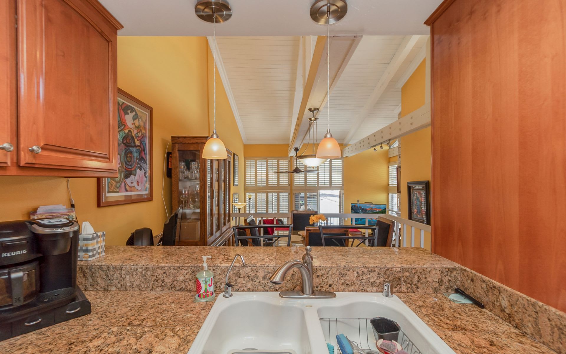 Kitchen with granite counters and a double sink overlooking a vaulted dining and living area.