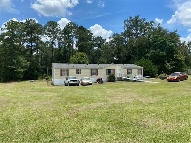 A single-story house in 88 Jubilee ln with a large, open front yard. The property has several cars parked in the yard and is surrounded by a mix of grass and trees.