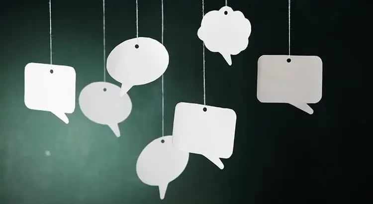 A collection of white speech bubbles hanging against a dark background, suggesting communication or social interaction.