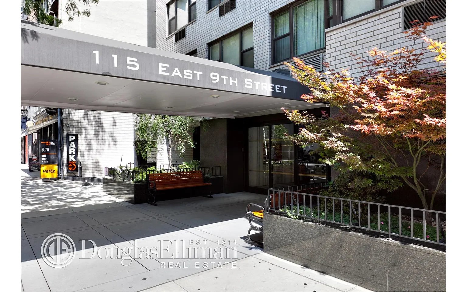 Entrance to 115 East 9th Street, marked by a wide canopy above a landscaped courtyard and benches.