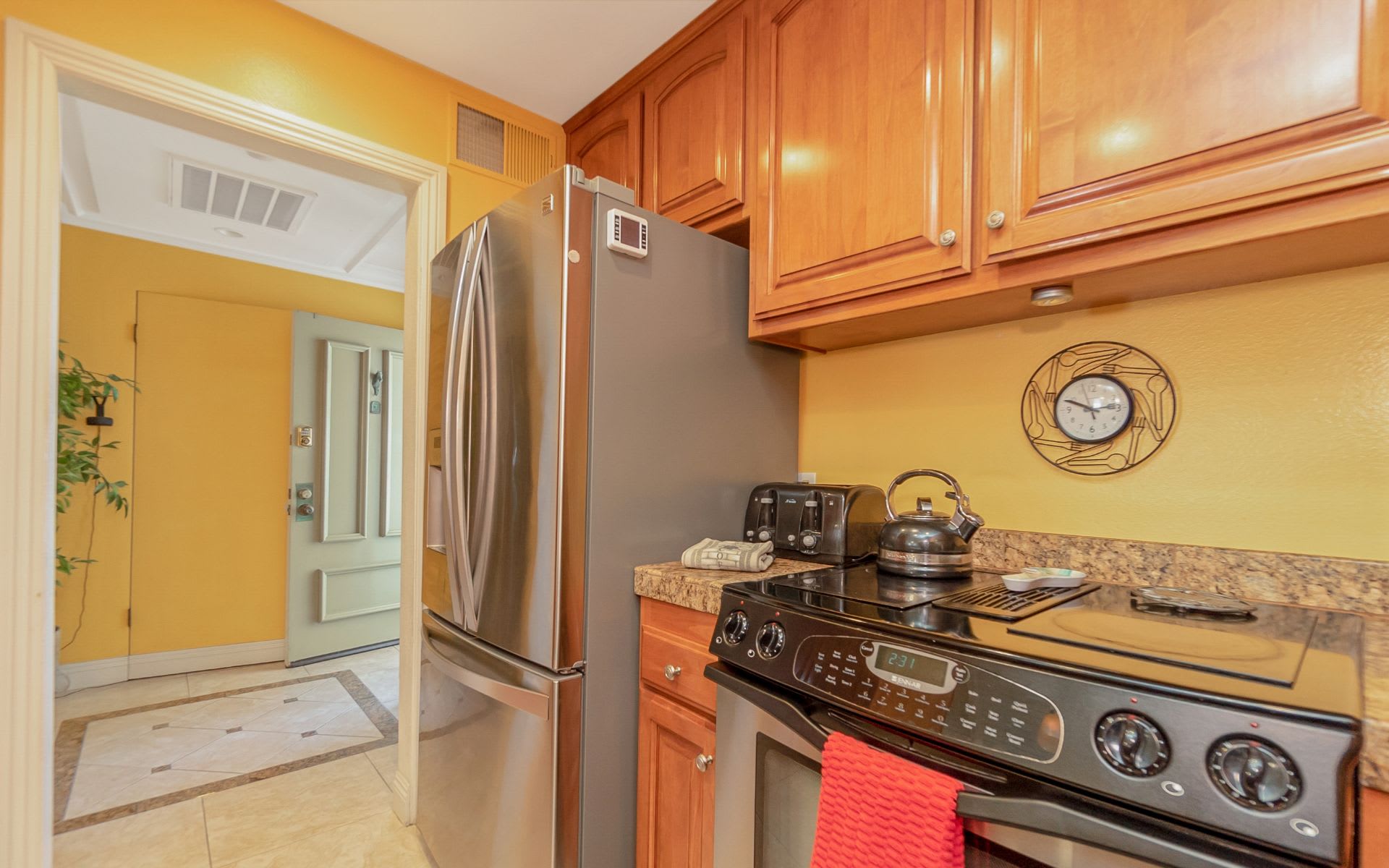 Kitchen with wood cabinets, granite counters, and stainless-steel appliances beside a tiled entryway.