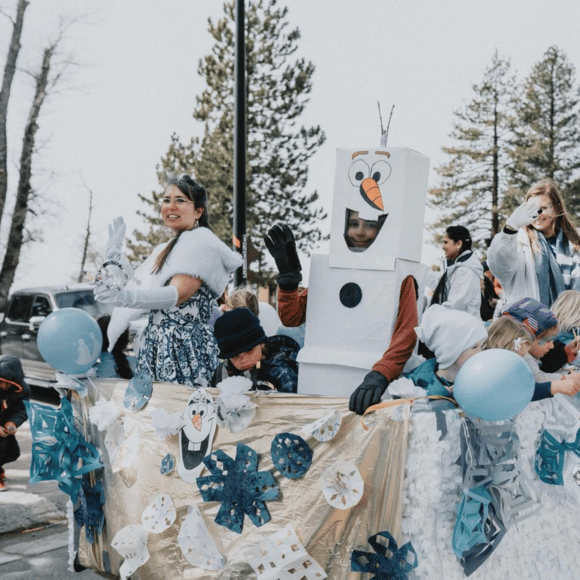 Winter parade float decorated in blue and white, with a person dressed as Olaf.