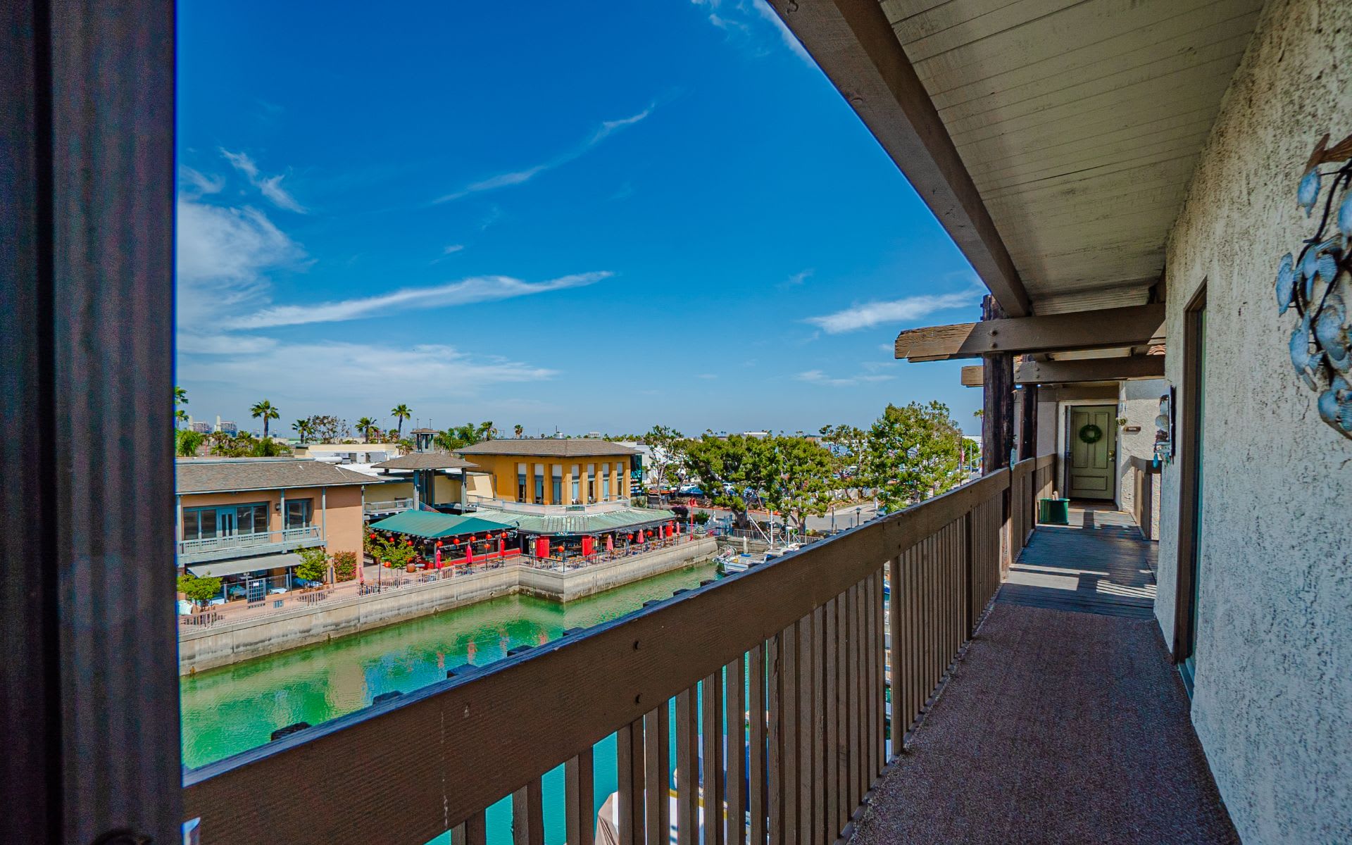 Covered balcony overlooks a canal and waterfront shops beneath a bright blue sky.