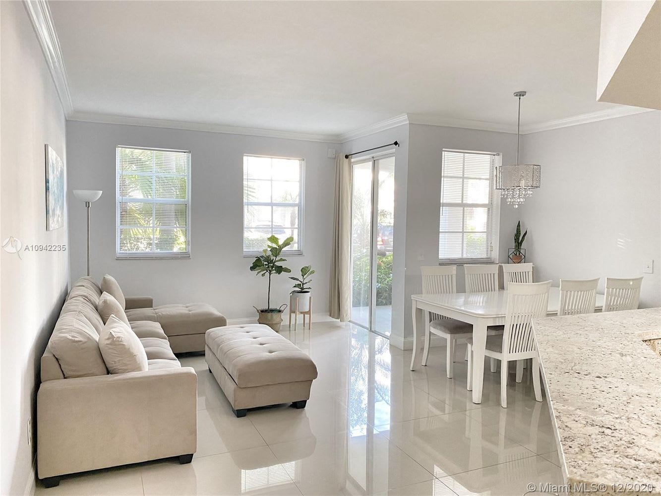 Open-plan living and dining room with a cream sectional, white dining set, and glossy tile floors.