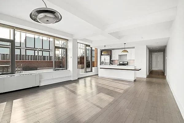 Vacant open-plan living area and kitchen with wide windows, wood floors, and a white island.