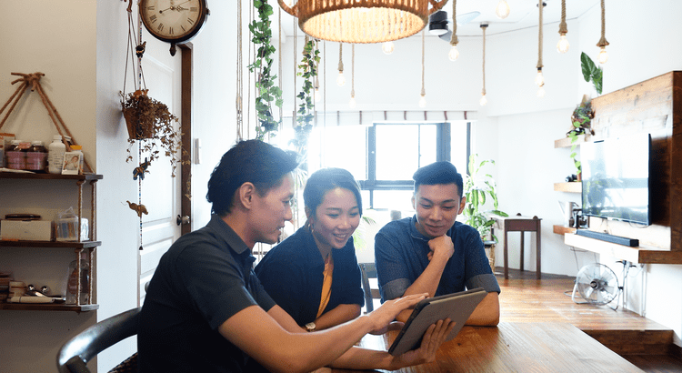 Three people having a discussion around a laptop in a well-decorated room, likely discussing real estate or financial planning.