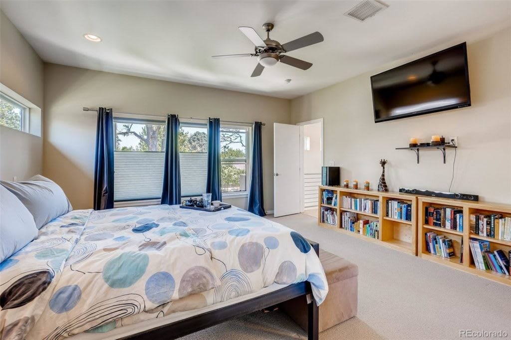 Bedroom with patterned bedding, navy curtains, a ceiling fan, and bookshelves.