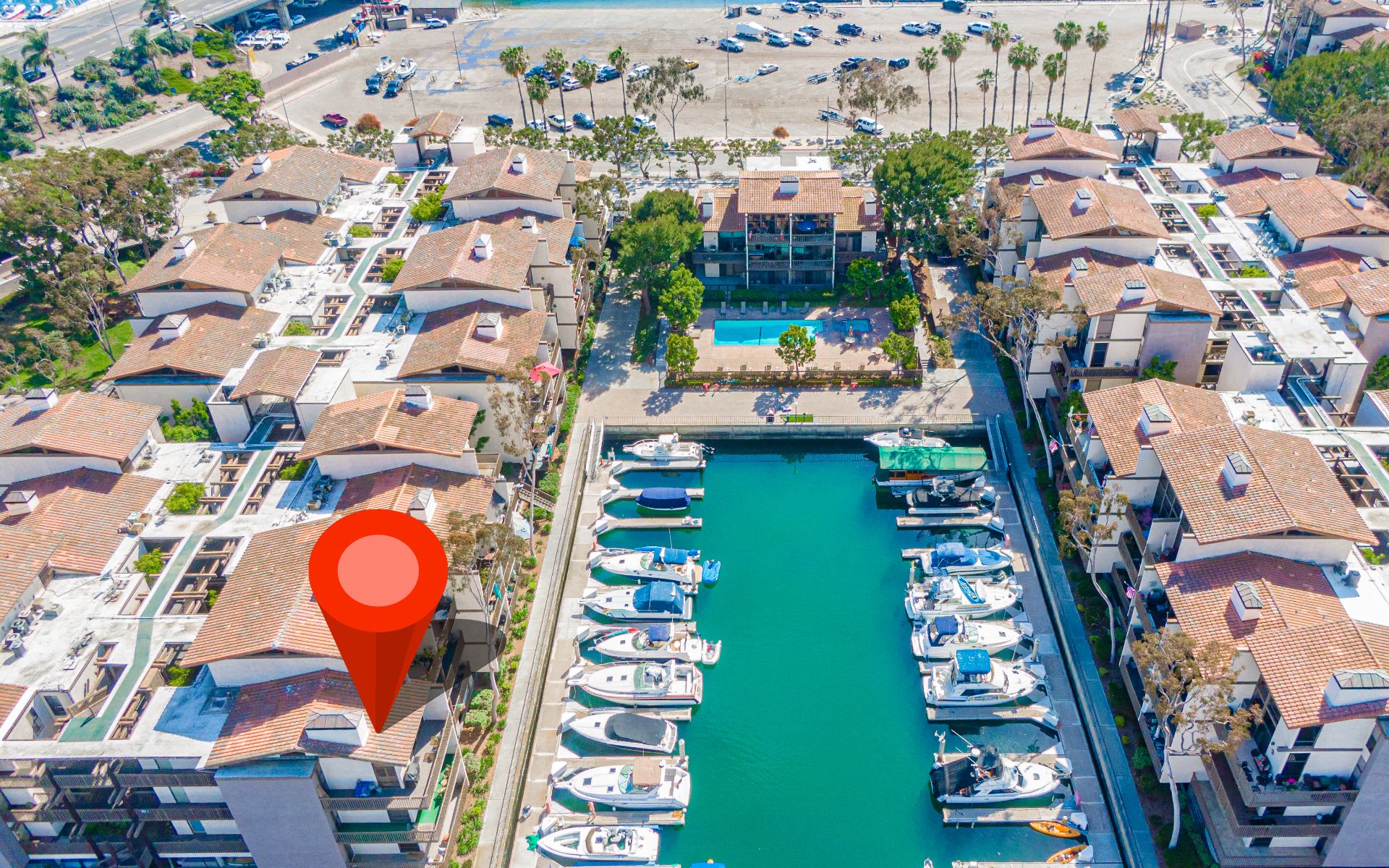 Aerial view of Marina Pacifica condos, with a boat-filled marina and pool; a red pin marks one unit.