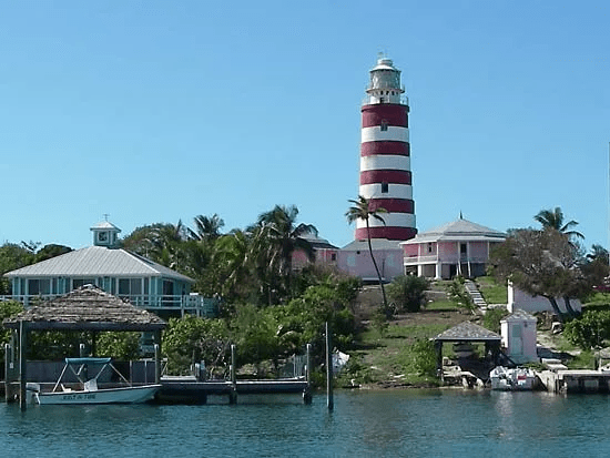 A red and white lighthouse sitting on a grassy hill overlooking a vast ocean.