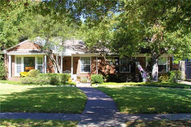 Single-story brick home shaded by mature trees, with a broad lawn and curved front walkway.