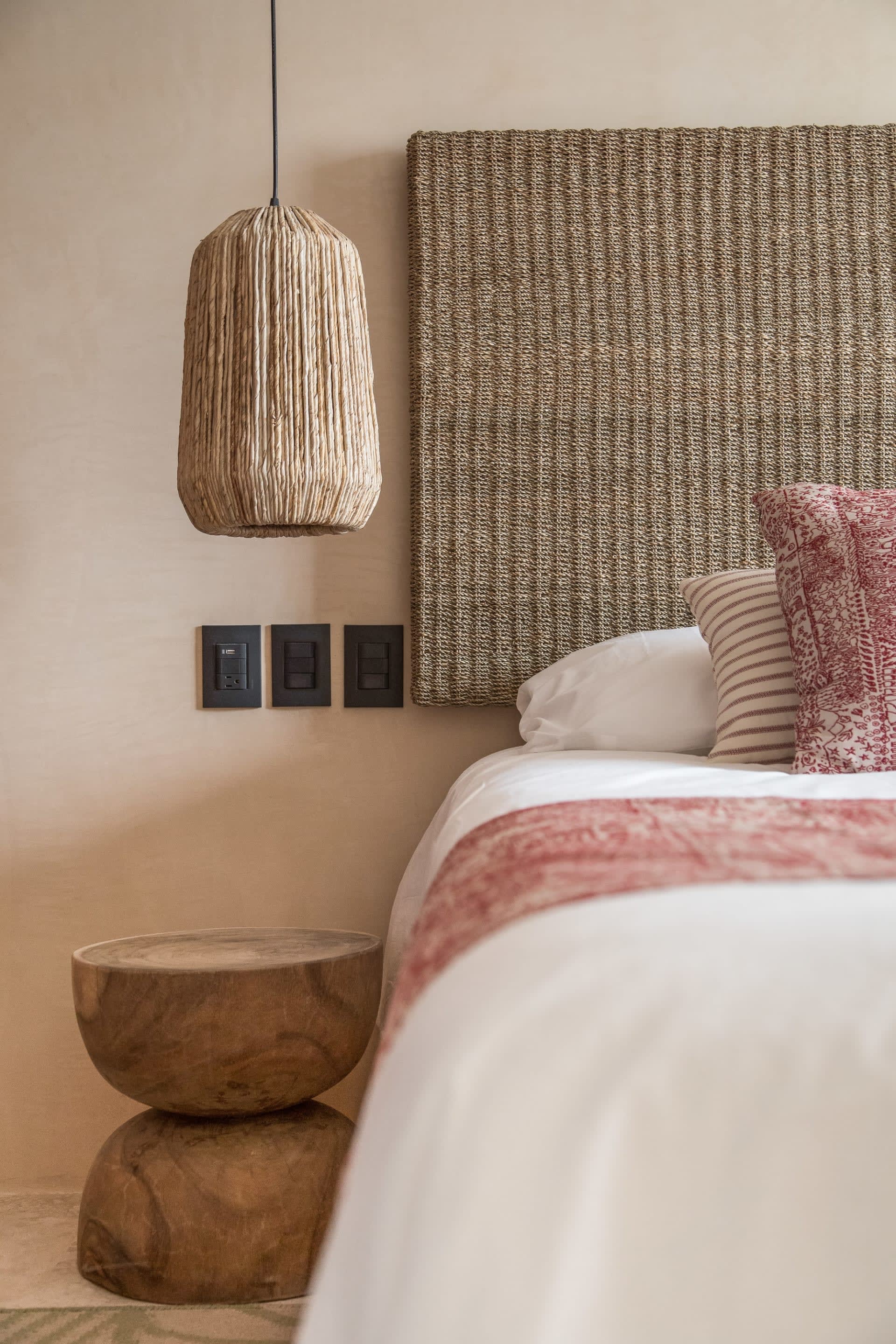 Bedroom with woven headboard, textured pendant light, rose-patterned bedding, and sculptural wooden bedside table.