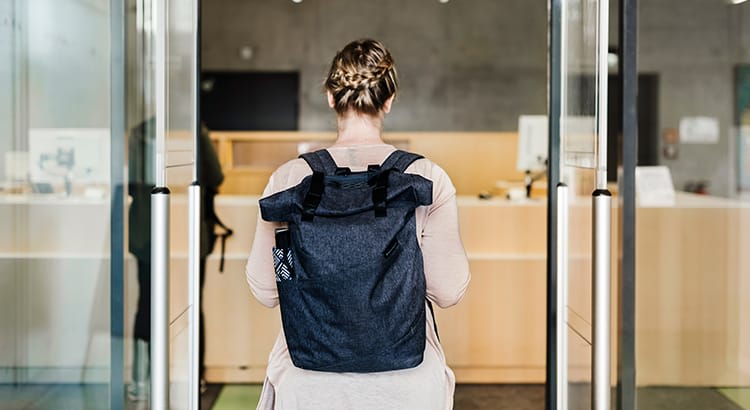 A person with a backpack, seen from behind, entering a modern building.