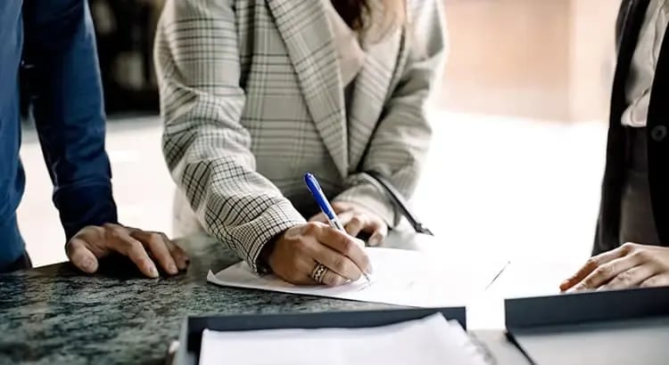  A person signing a document, with another person in the background.
