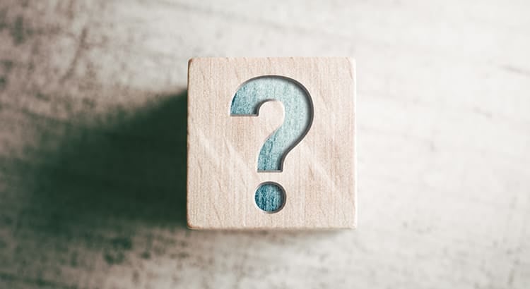 A wooden block with a question mark on it, set on a neutral background.