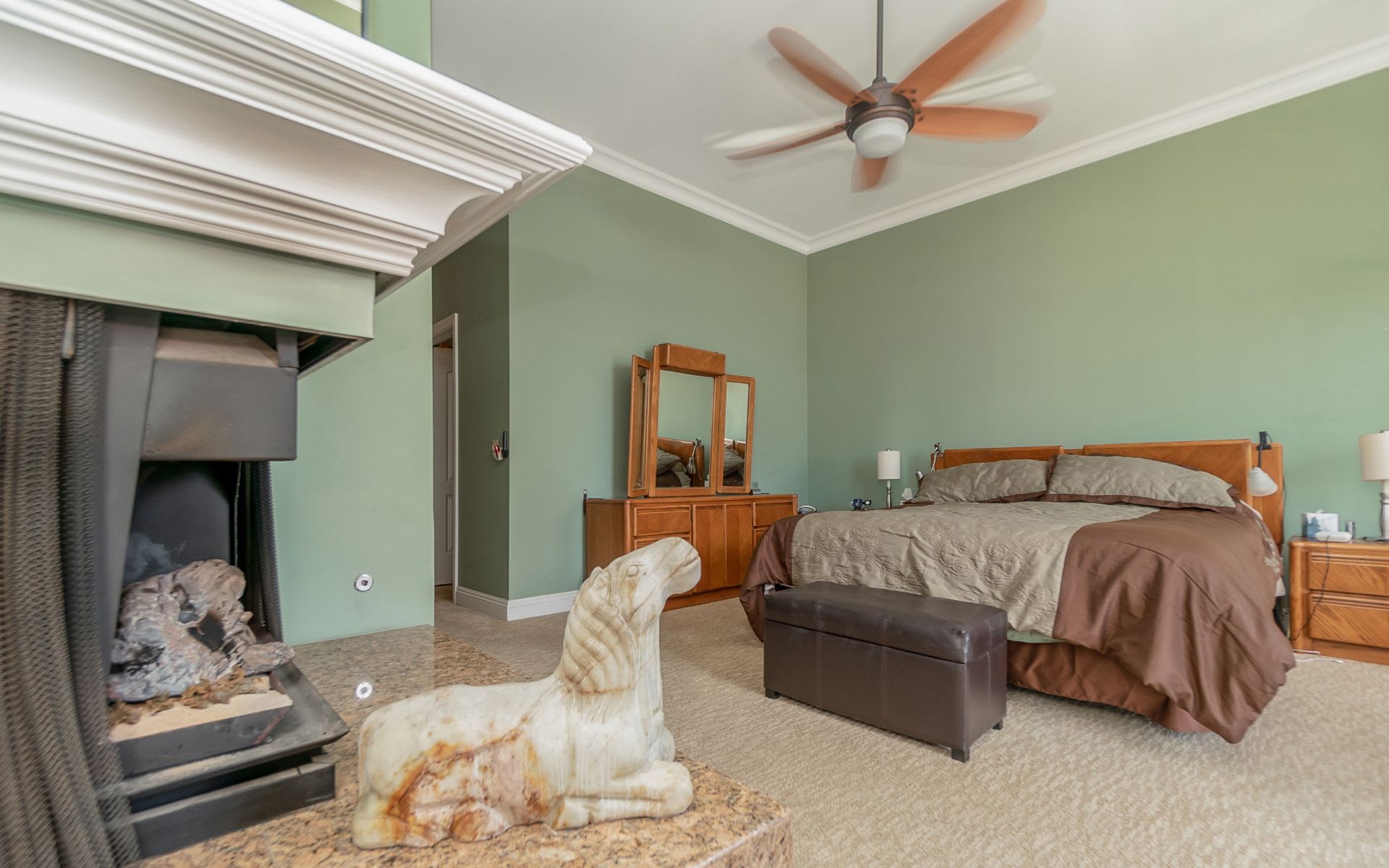 Bedroom with a wooden bed, green walls, fireplace, and carved stone dog sculpture on the hearth.