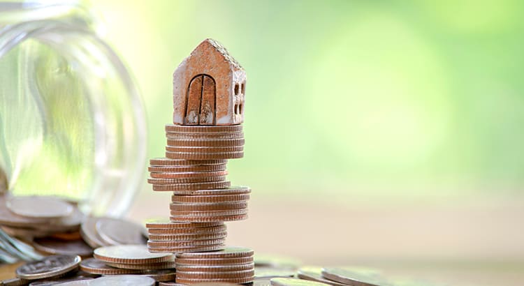 A conceptual image showing a small house model on top of a stack of coins, symbolizing financial investment or real estate.