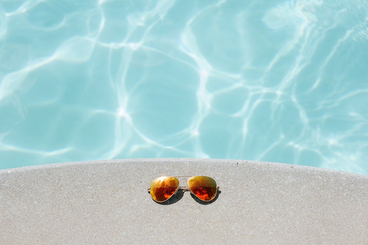 Amber aviator sunglasses on a concrete pool edge beside turquoise water.