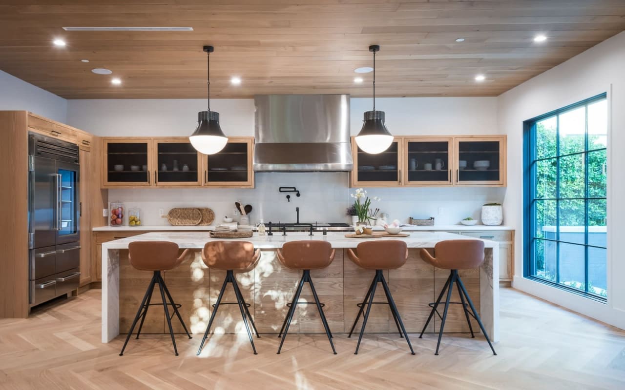 Modern kitchen with wood accents, large island with leather stools, marble countertop, and warm, inviting atmosphere.