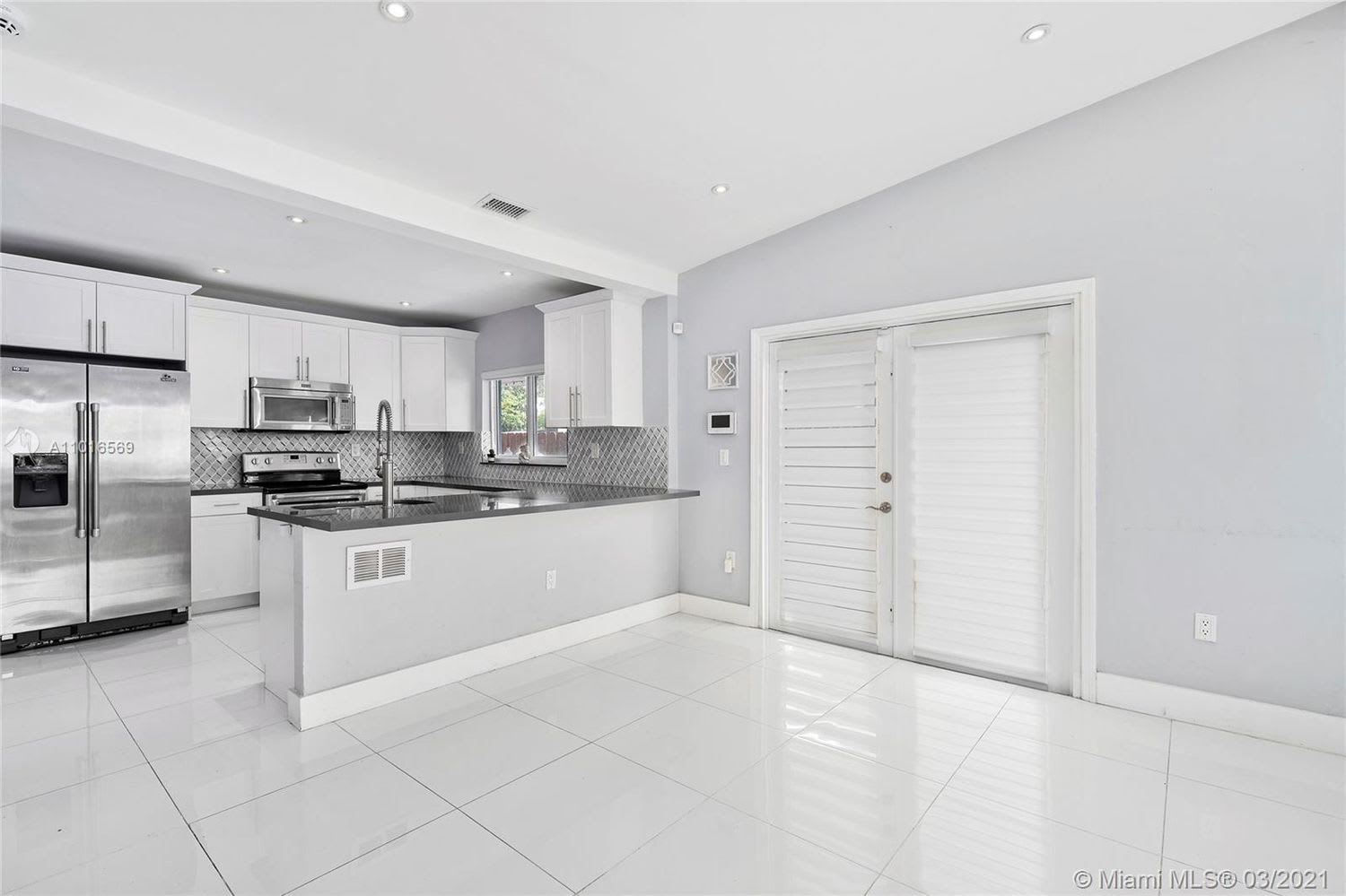 Bright kitchen with white cabinets, stainless appliances, gray tile backsplash, and a wide island.