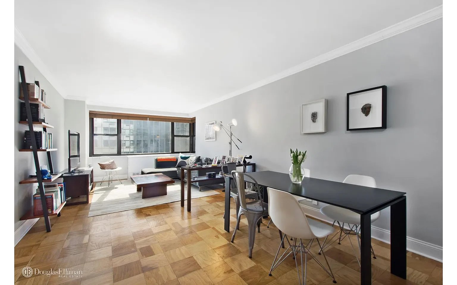 Living and dining area with parquet floors and large windows overlooking neighboring buildings.